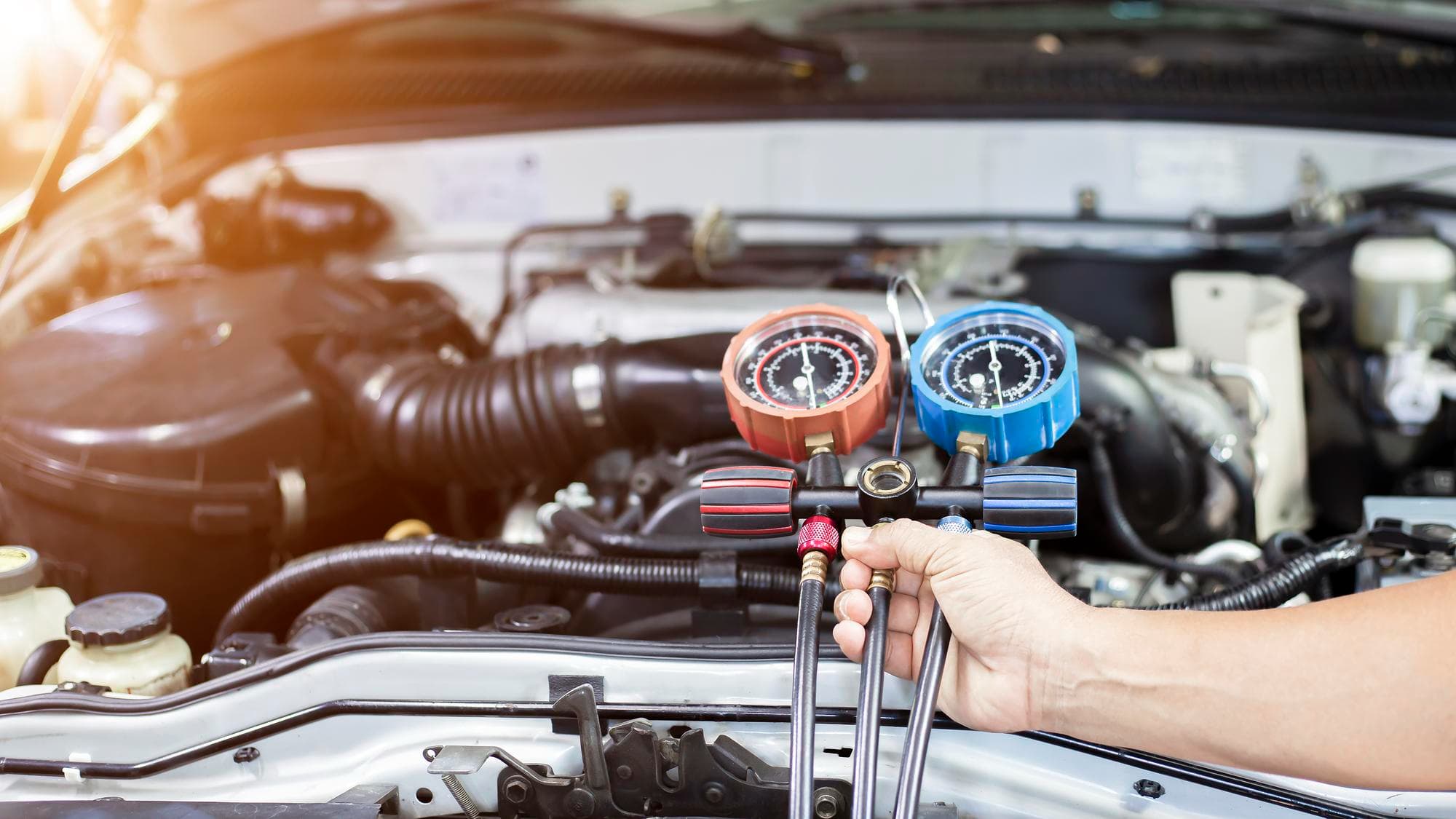 Mechanic using AC manifold gauge set to check car air conditioning system pressure under hood