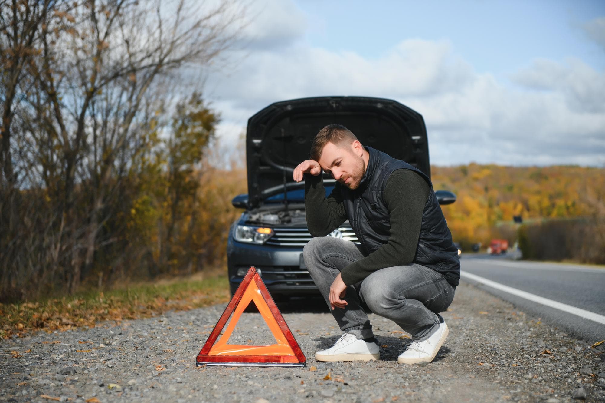 Check Engine Light On Frustrated driver next to car with hood open on roadside, warning triangle placed in front for safety